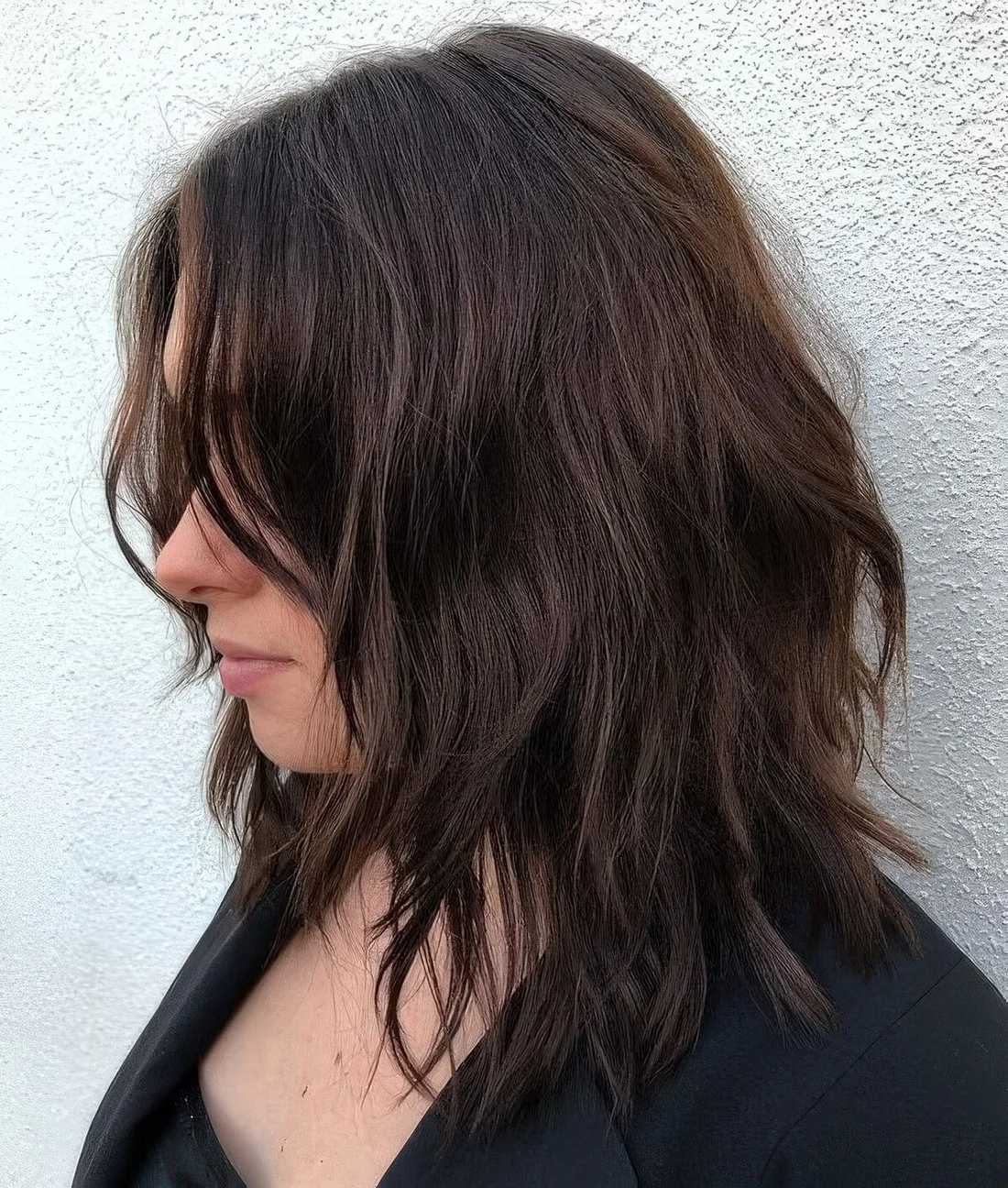 Dark brown choppy medium haircut with side bangs and messy waves shows off some texture and dimension.