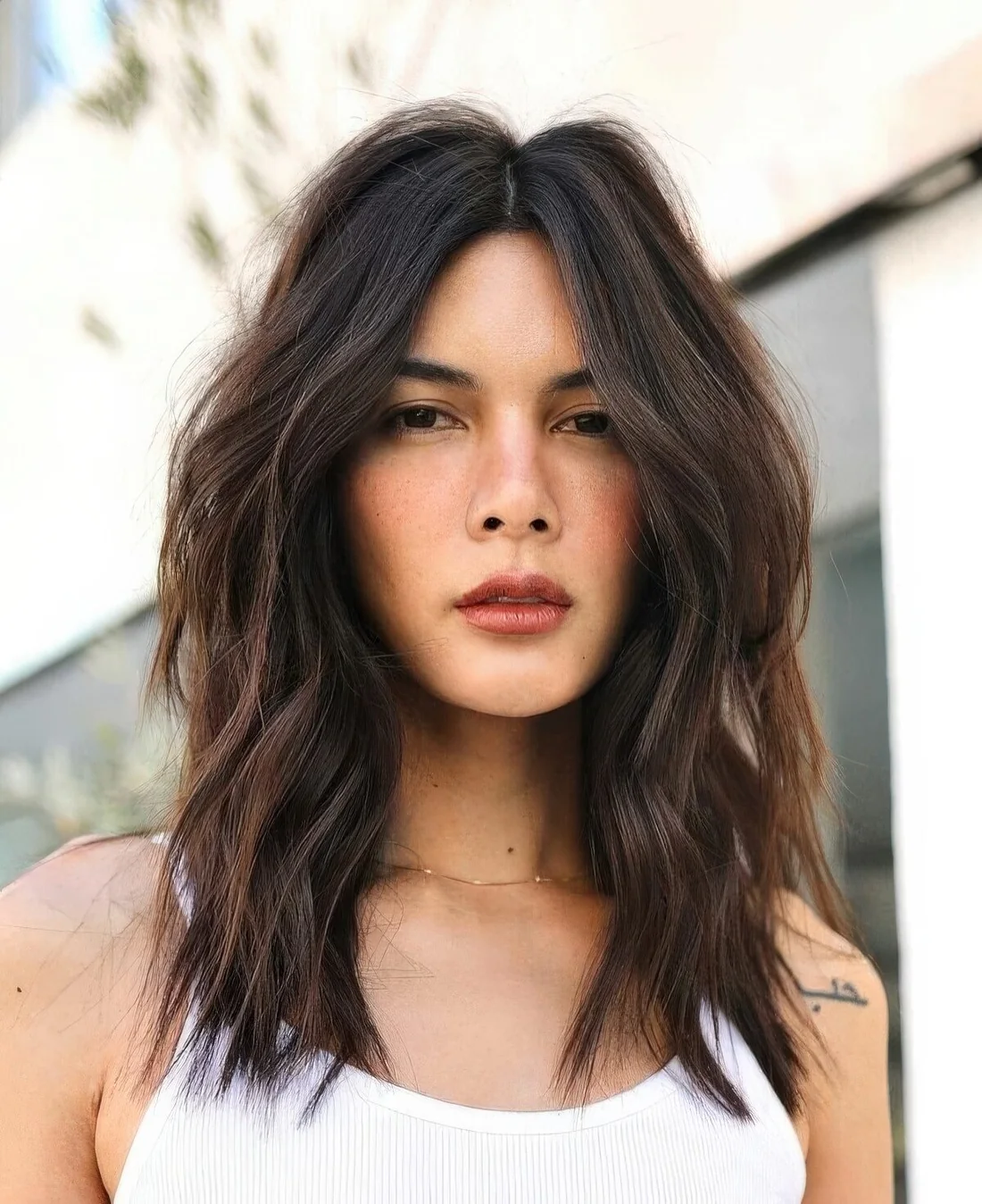 Dark brown center-parted textured lob with caramel balayage and slight waves plus a lot of volume.