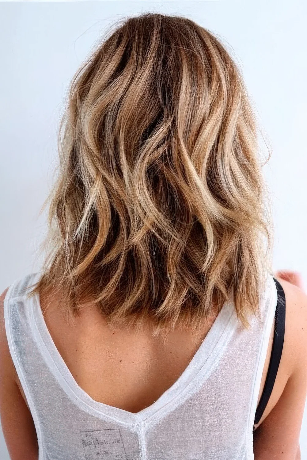Beach hairstyle with medium-length bronde hair, blonde highlights and waves.