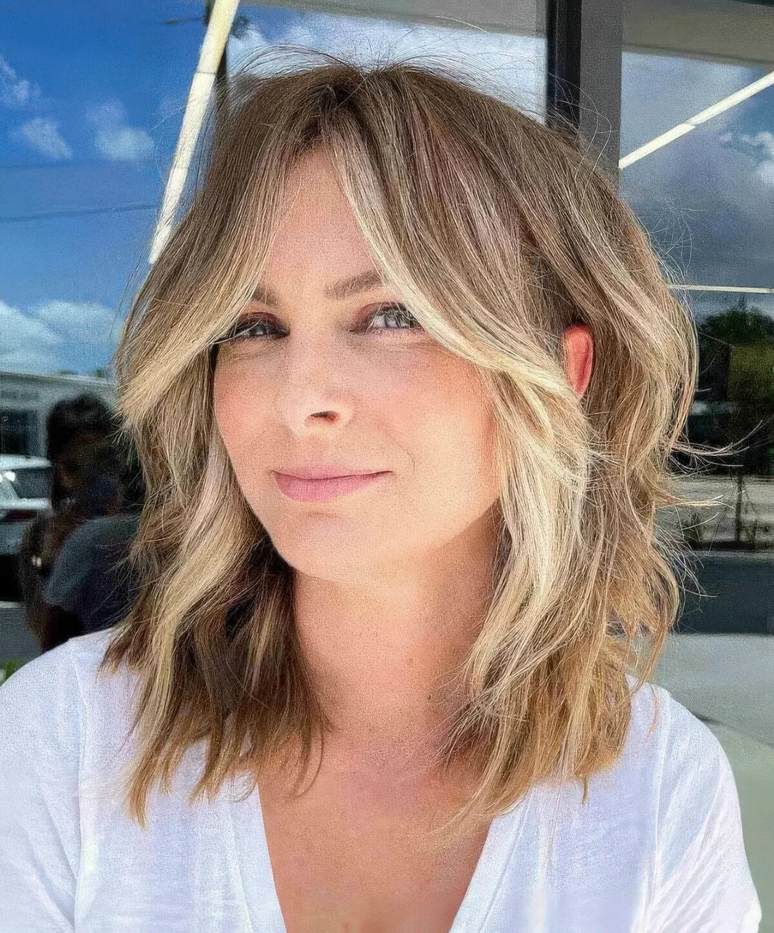 Flattering face-framing wavy lob with curtain bangs and blonde highlights and money piece.