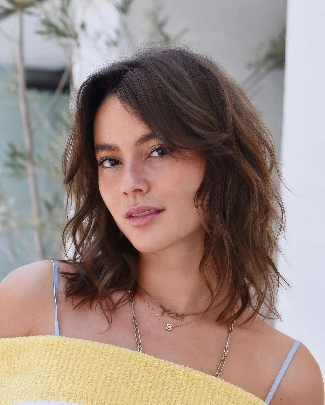Brown medium-length hairstyle with caramel balayage, waves and curtain bangs to frame the face.