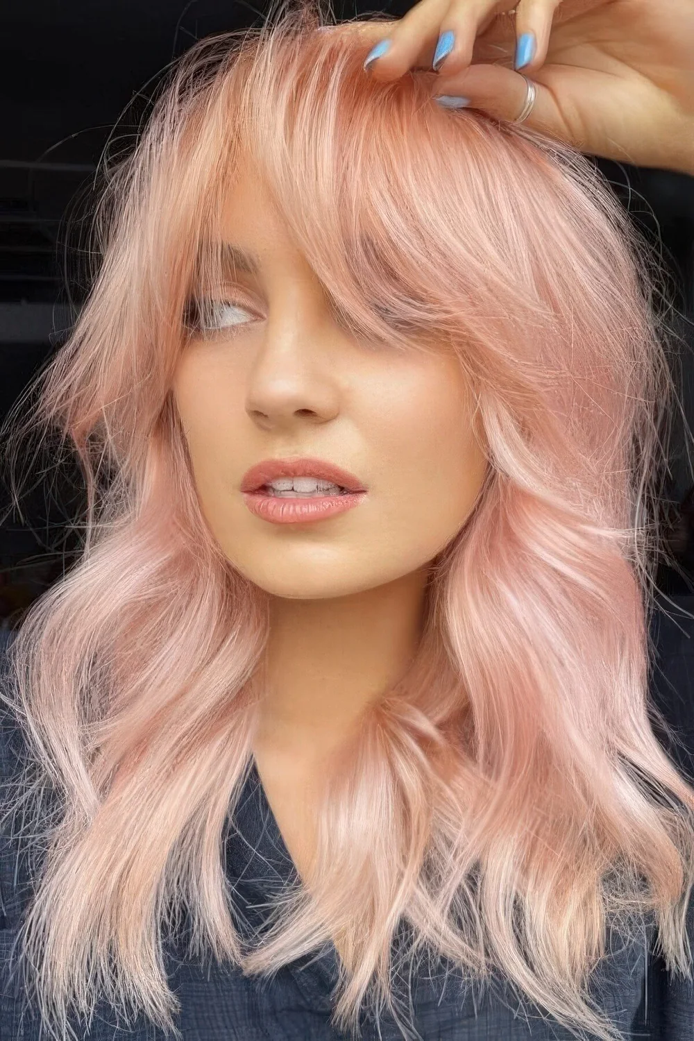 Peachy pink shoulder-length hair with a lot of volume and waves and bottleneck bangs.