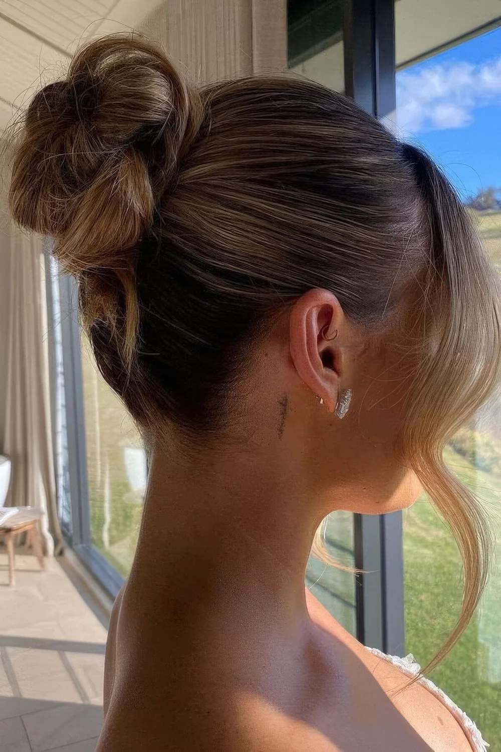 Chic wrapped top bun with a sleek and tight top and some face frmaing hair.
