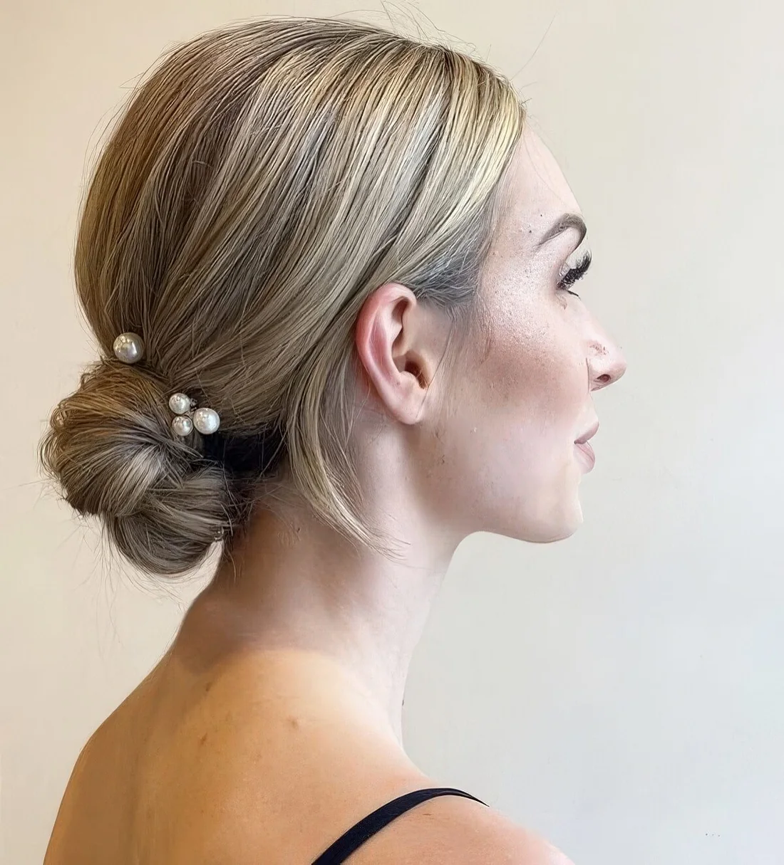 Wrapped low bun with a sleek top and pearl hairpins.