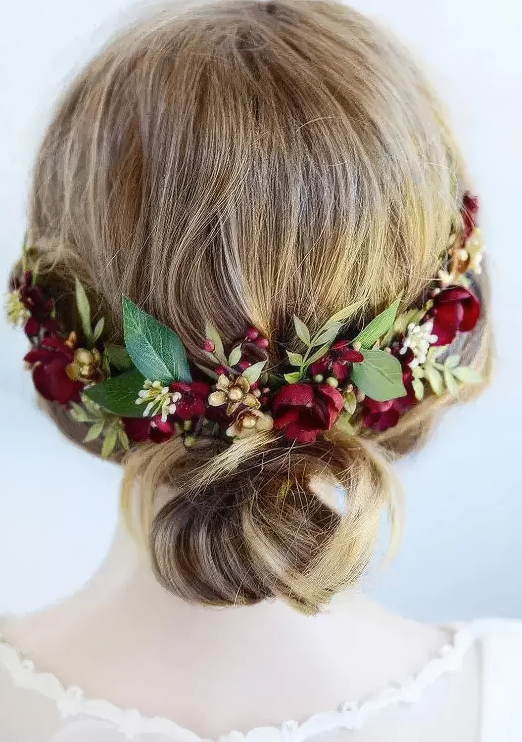 Wedding low bun on medium-length hair accented with burgundy blooms and greenery.