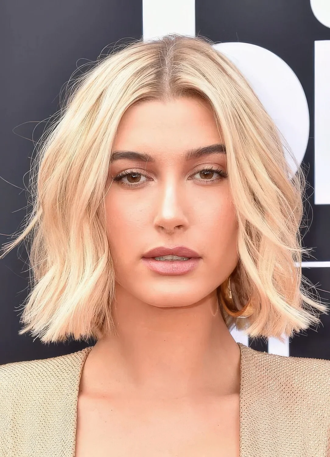 Hailey Bieber wearing a wavy blonde midi bob with center part.