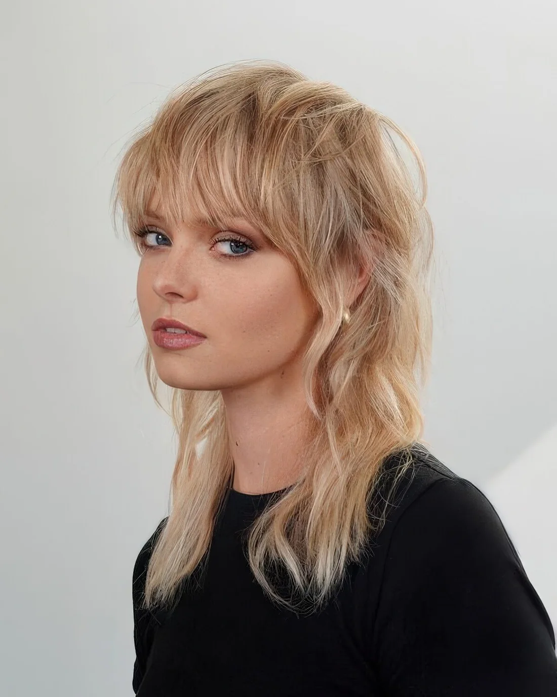 Long mullet with delicate shades of blonde, with mesys bangs and long sides and back.