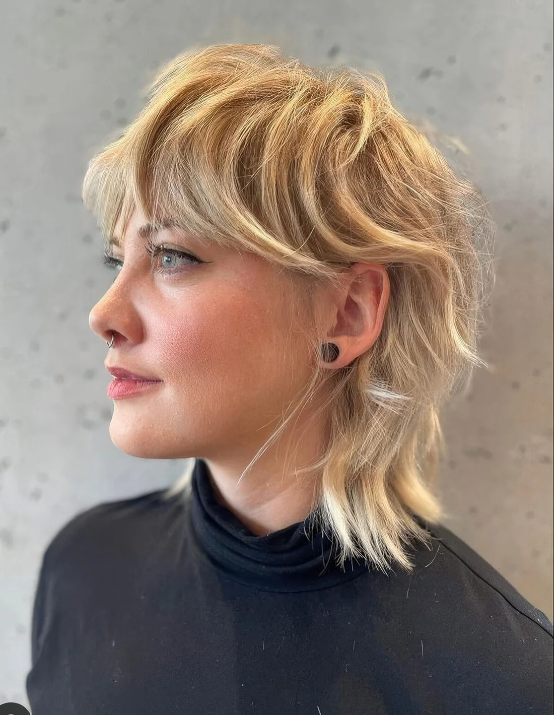 Textural mullet n blonde shades, with bangs, longer hair on top and shorter hair on the sides and back.
