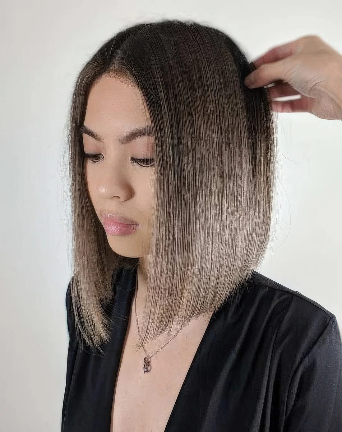Mousy brown angled bob haircut with center part and an ombre effect from darker root to mousy brown on the ends.