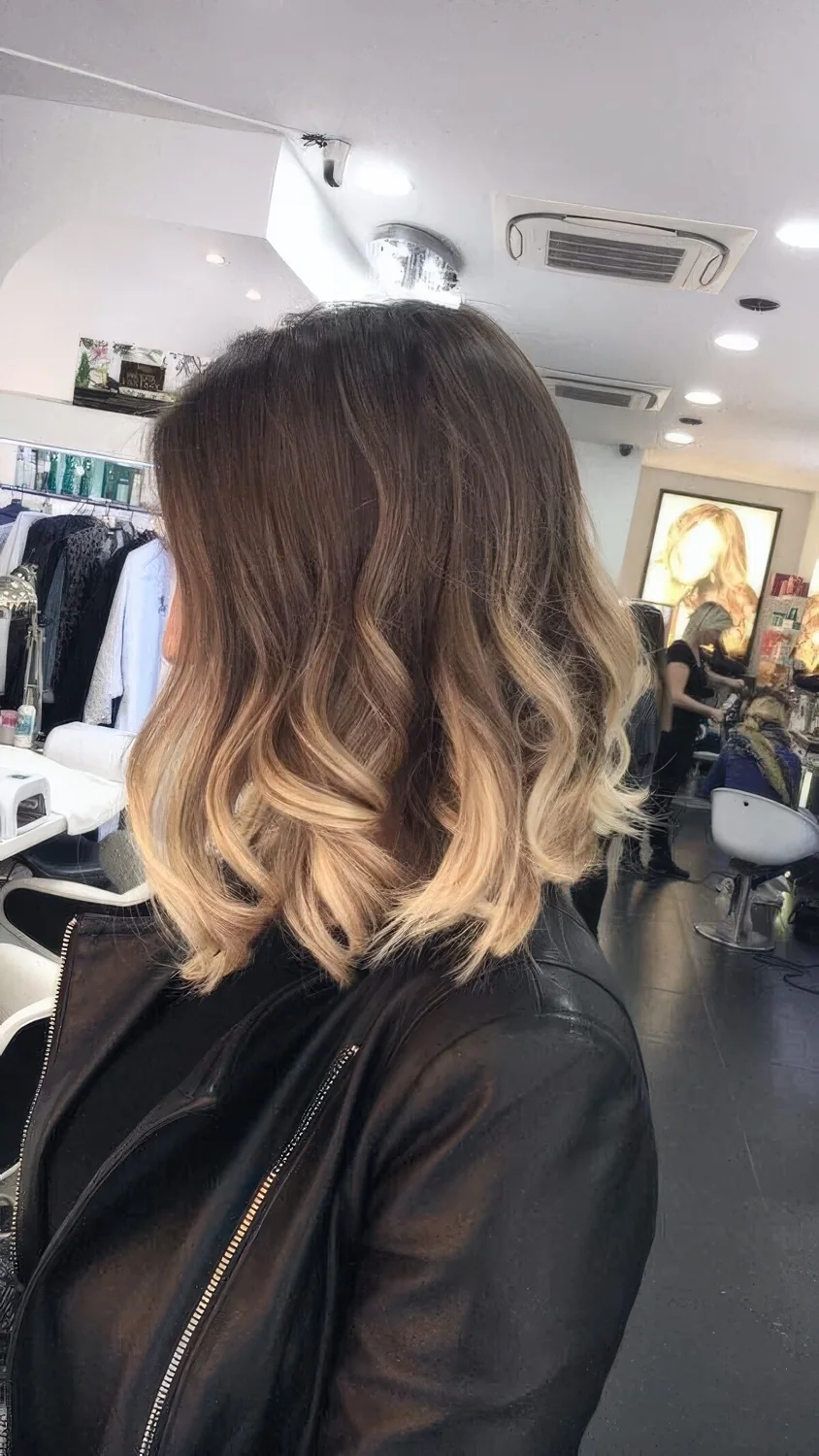 Layered long bob with an ombre effect, from brunette to bleached blonde, with waves and volume.