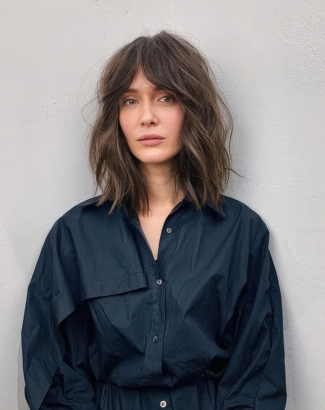 Brown outgrown bob with slight highlights, messy waves and bottleneck bangs.