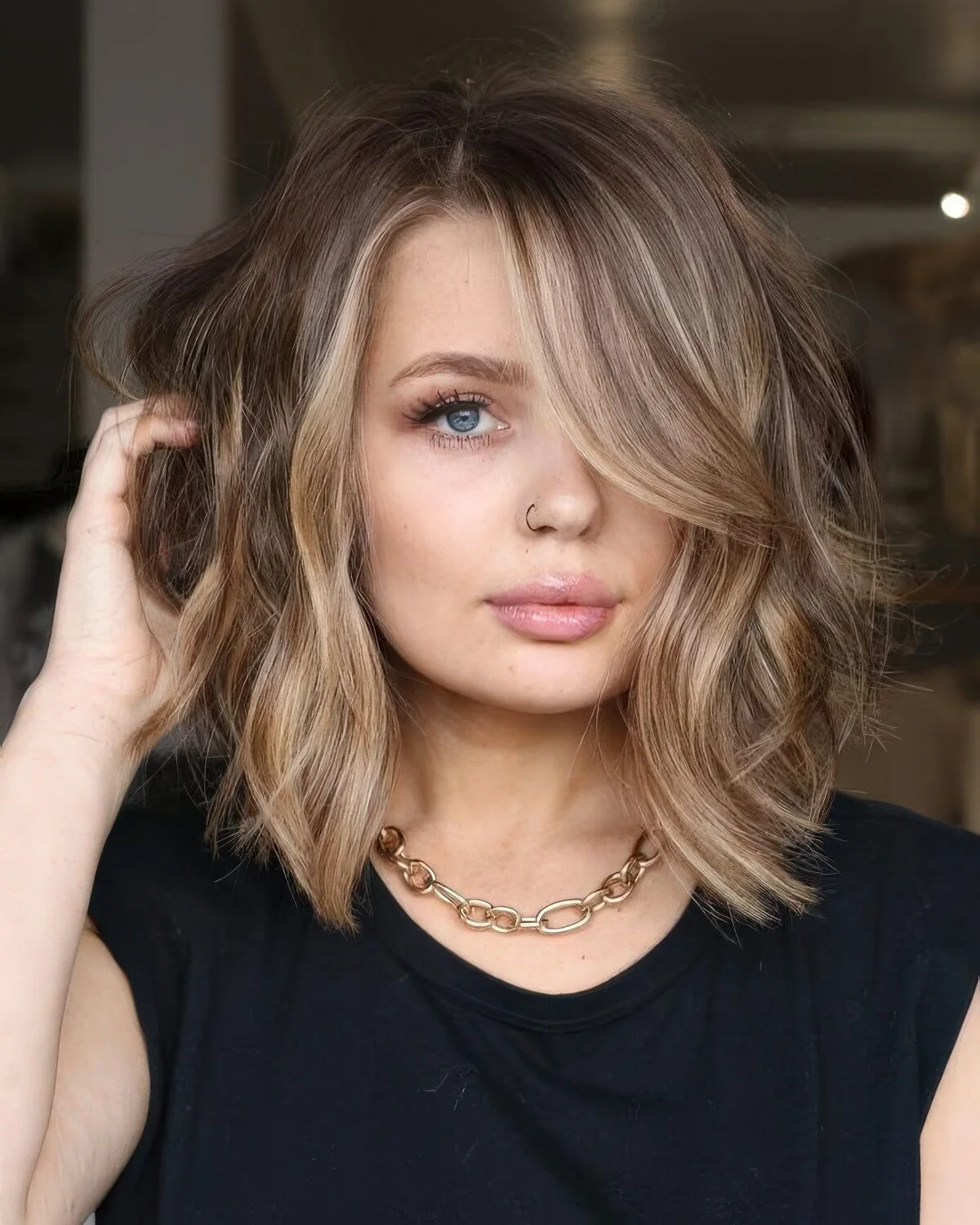 Light brown textural and wavy outgrown bob with side part and blonde balayage.