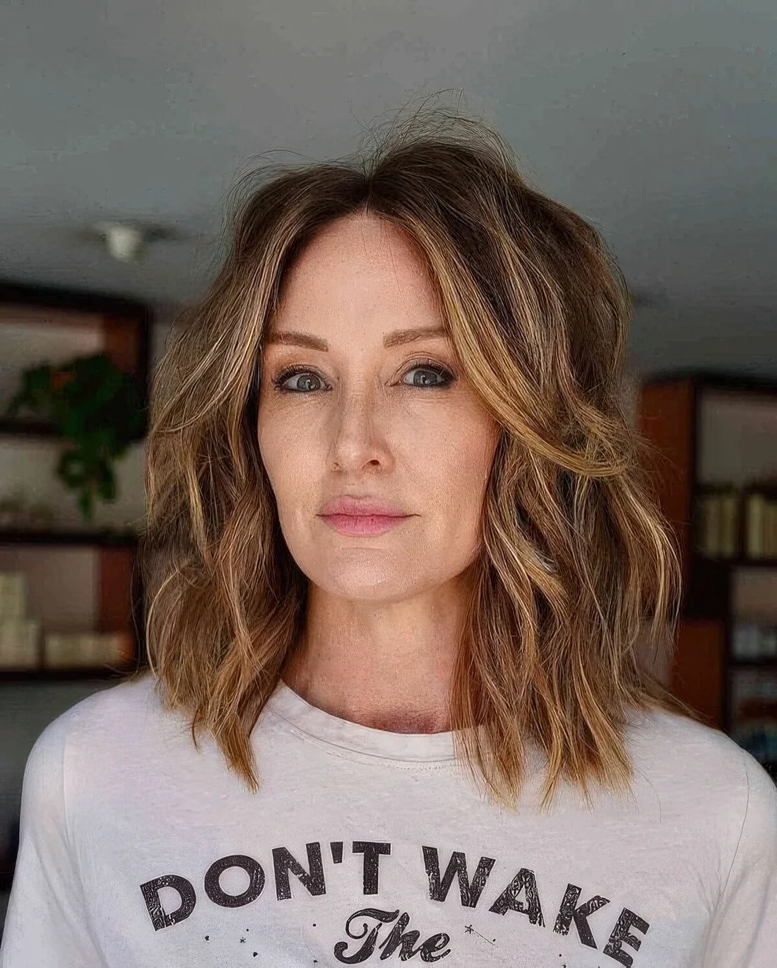 Wavy and shaggy outgrown bob in light brown and with honey highlights, with a lot of volume and center part.