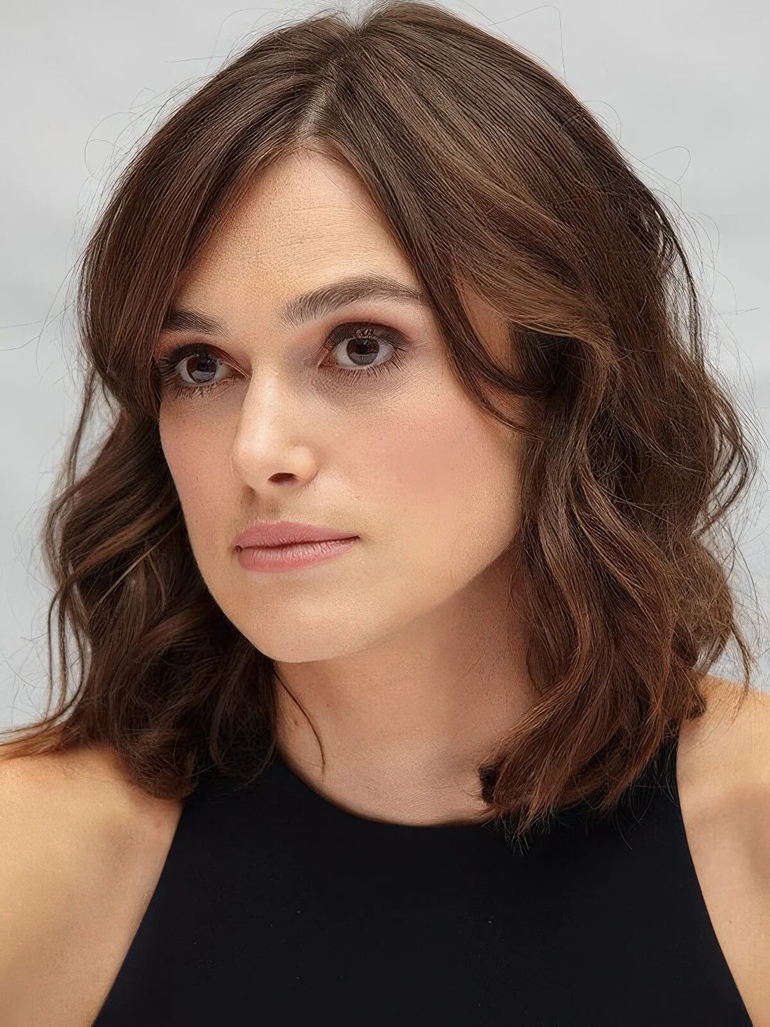 Keira Knightley wearing a brown wavy outgrown bob with side part and side bangs.