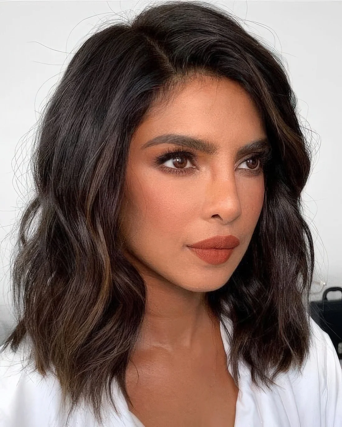 Priyanka Chopra wearing a black wavy outgrown bob with caramel highlights and side part plus a lot of volume.