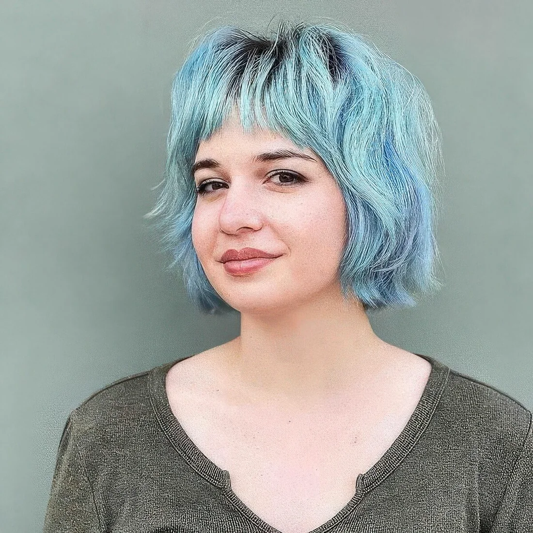 Pastel blue and green shaggy messy bob with wispy bangs, a darker root and a lot of wavy volume.