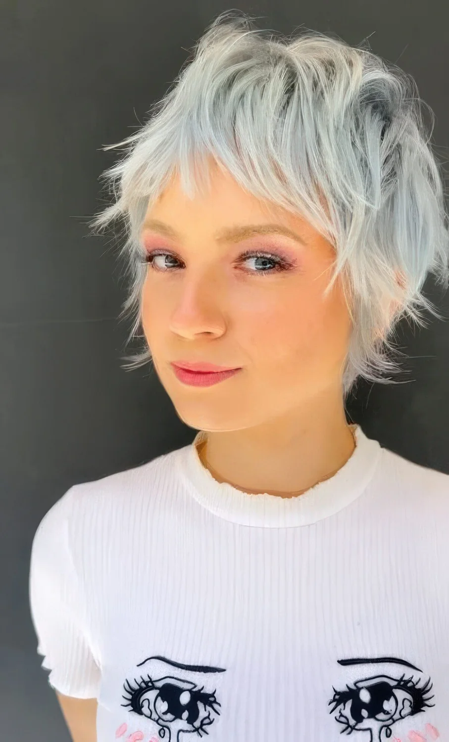 Long and messy pale blue pixie cut with a touch of mullet, with bangs and a lot of volume and texture.