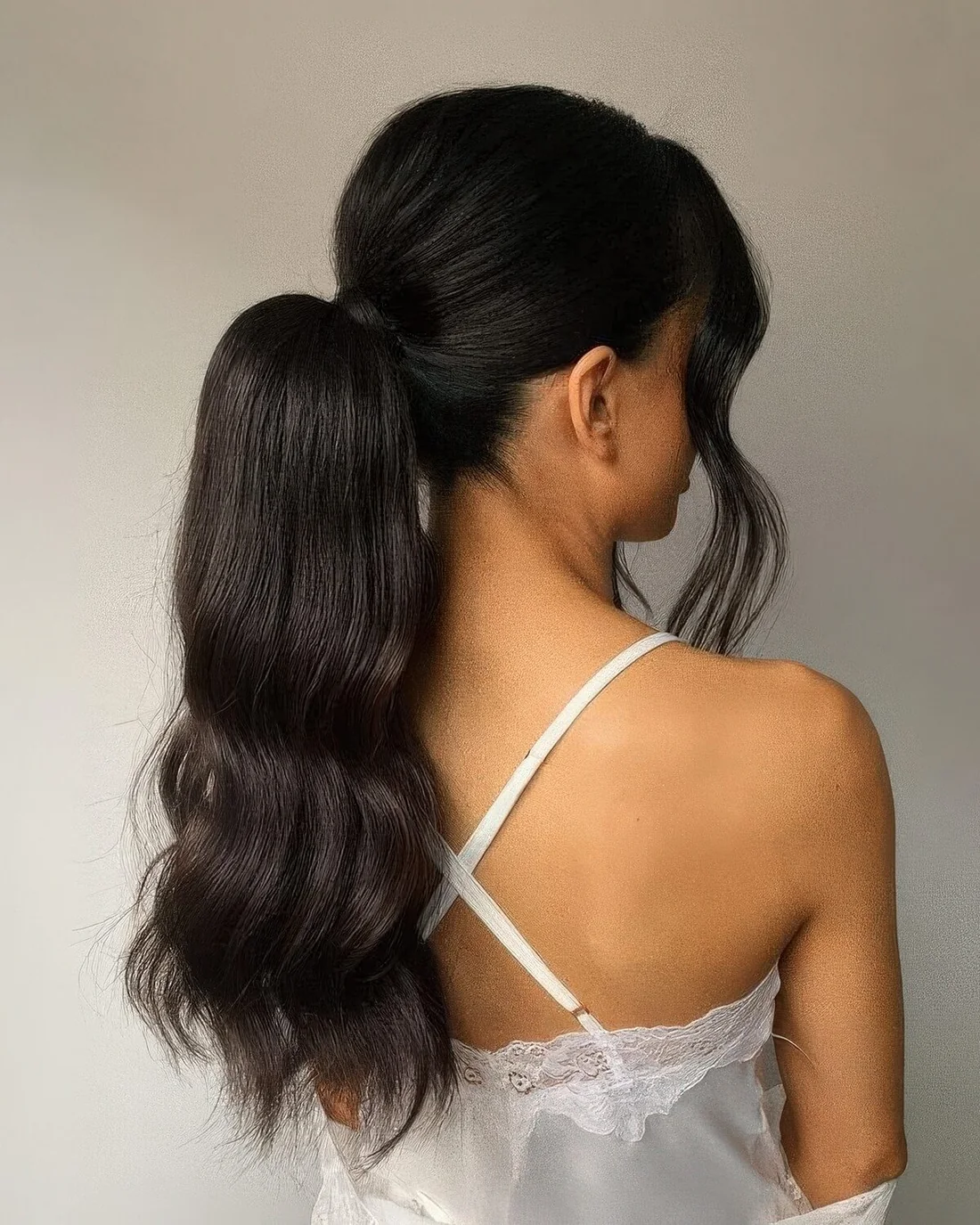 Wavy volumetric midi ponytail with a bump on top and long and wavy curtain bangs.