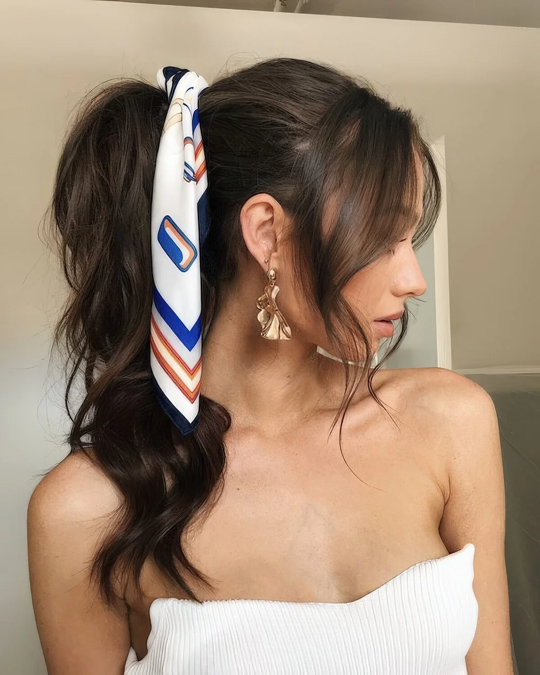 Ponytail with a volume on top and face-framing hair, with a colorful head scarf accenting the hairstyle for a fun and bodl touch.