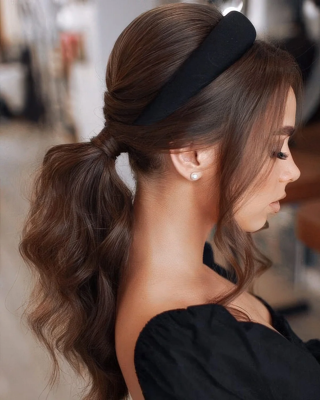 Long wavy ponytail, a bump on top and extra long curtain bangs plus a black padded headband for an accent.