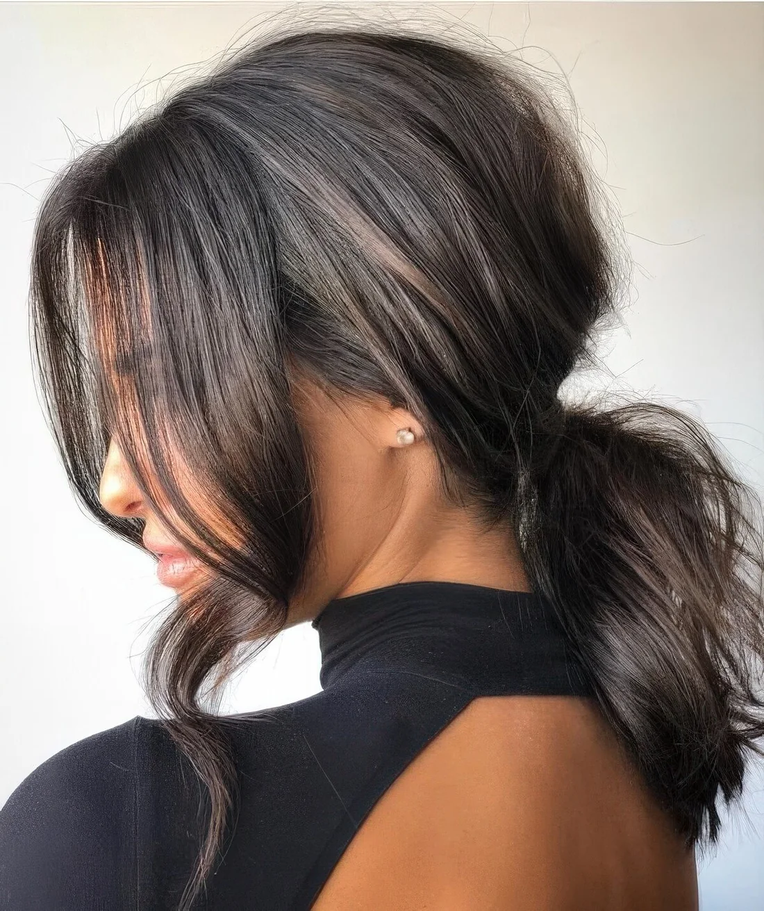 Low messy and wavy ponytail, with a bump on top and long wavy curtain bangs are a lovely and chic combo for a party or every day.