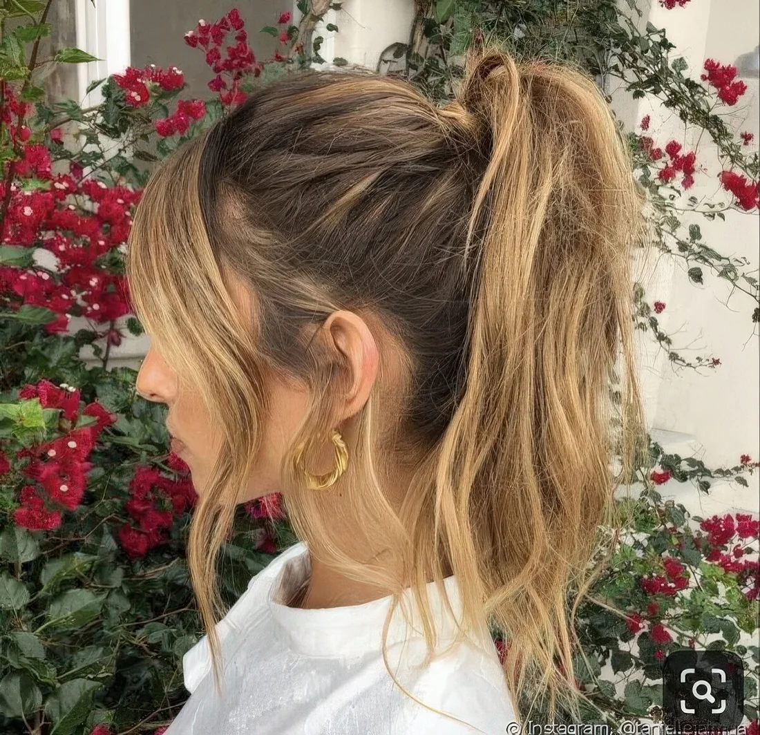 Messy textural high ponytail with a bump on top and wavy curtain bangs to accent the face.