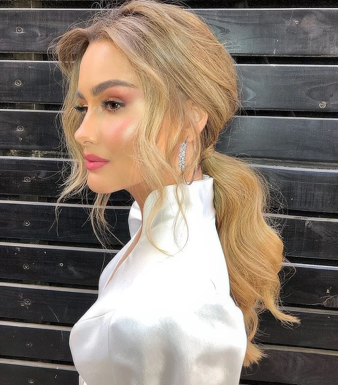 Messy wavy low ponytail with a bump on top and wavy curtain bangs are a chic and refined combo for a many occasions.