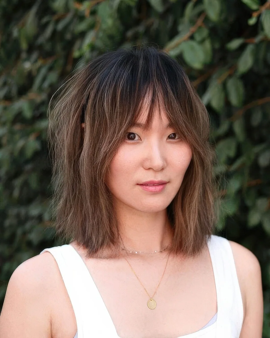 Brunette outgrown bob in brunette and with a dark root, with a shaggy texture and dimension.