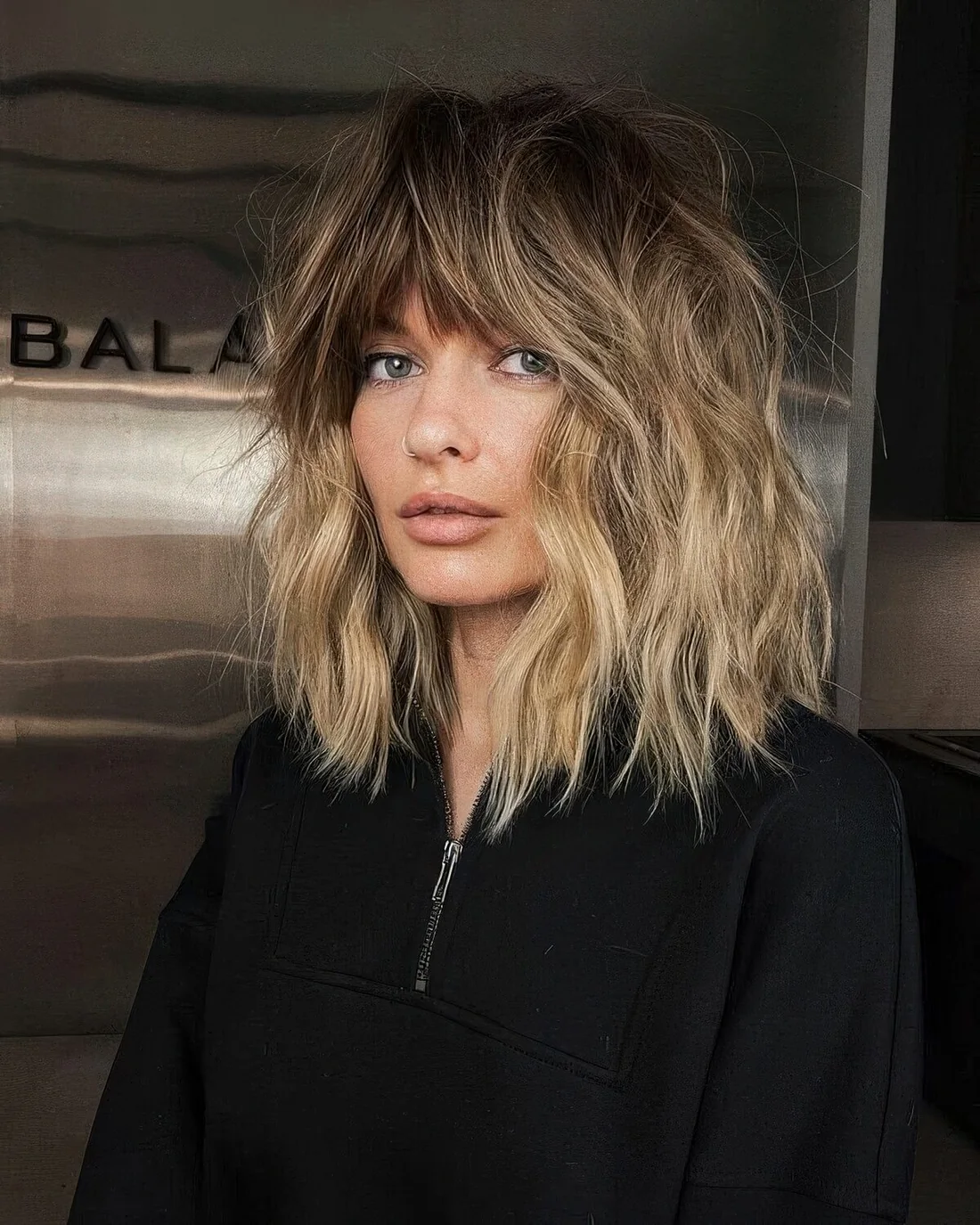 Dimensional outgrown bob haircut with a darker root, blonde balayage and a fringe.