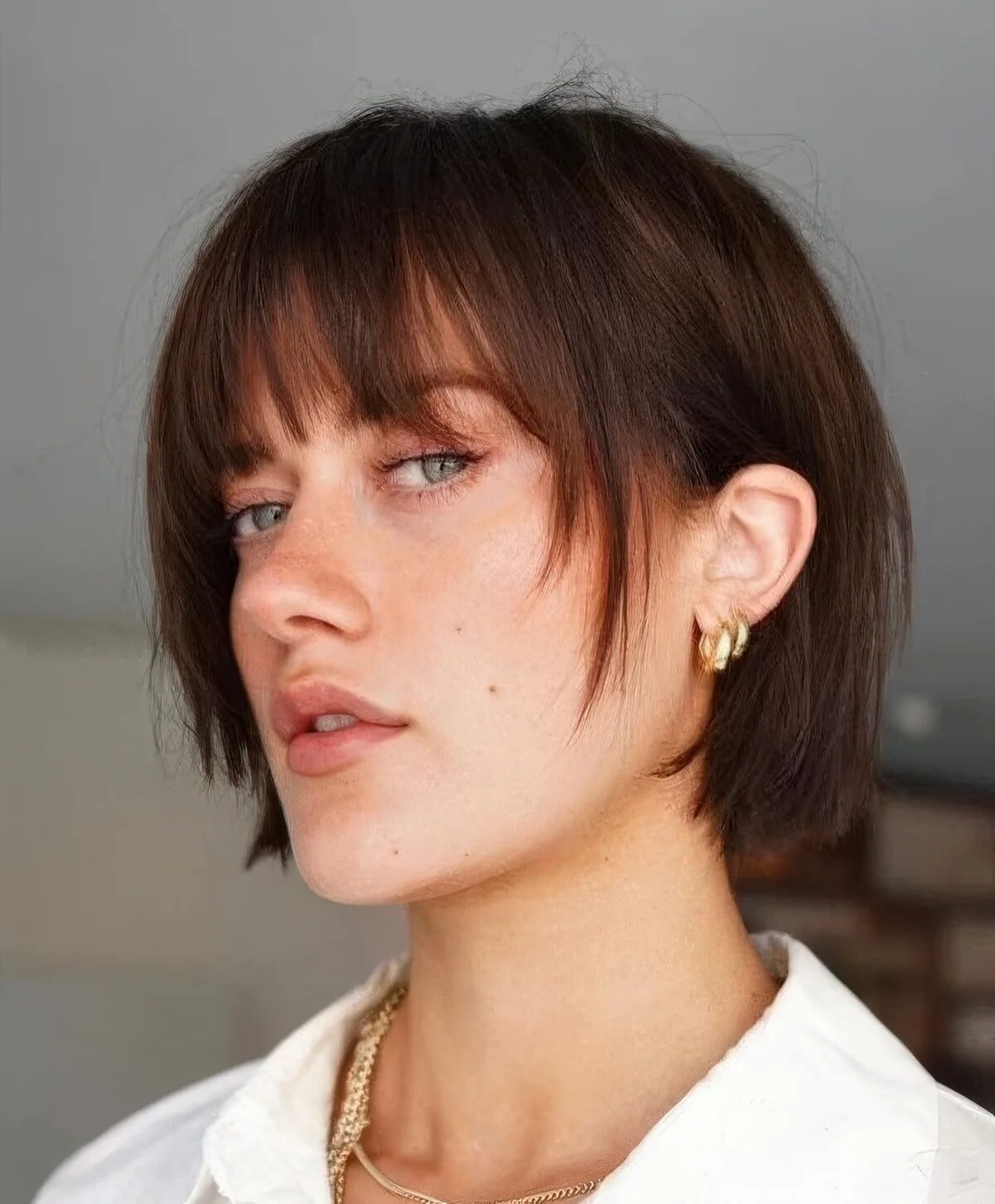 Blunt dark brunette bob with wispy bangs and face-framing layers.