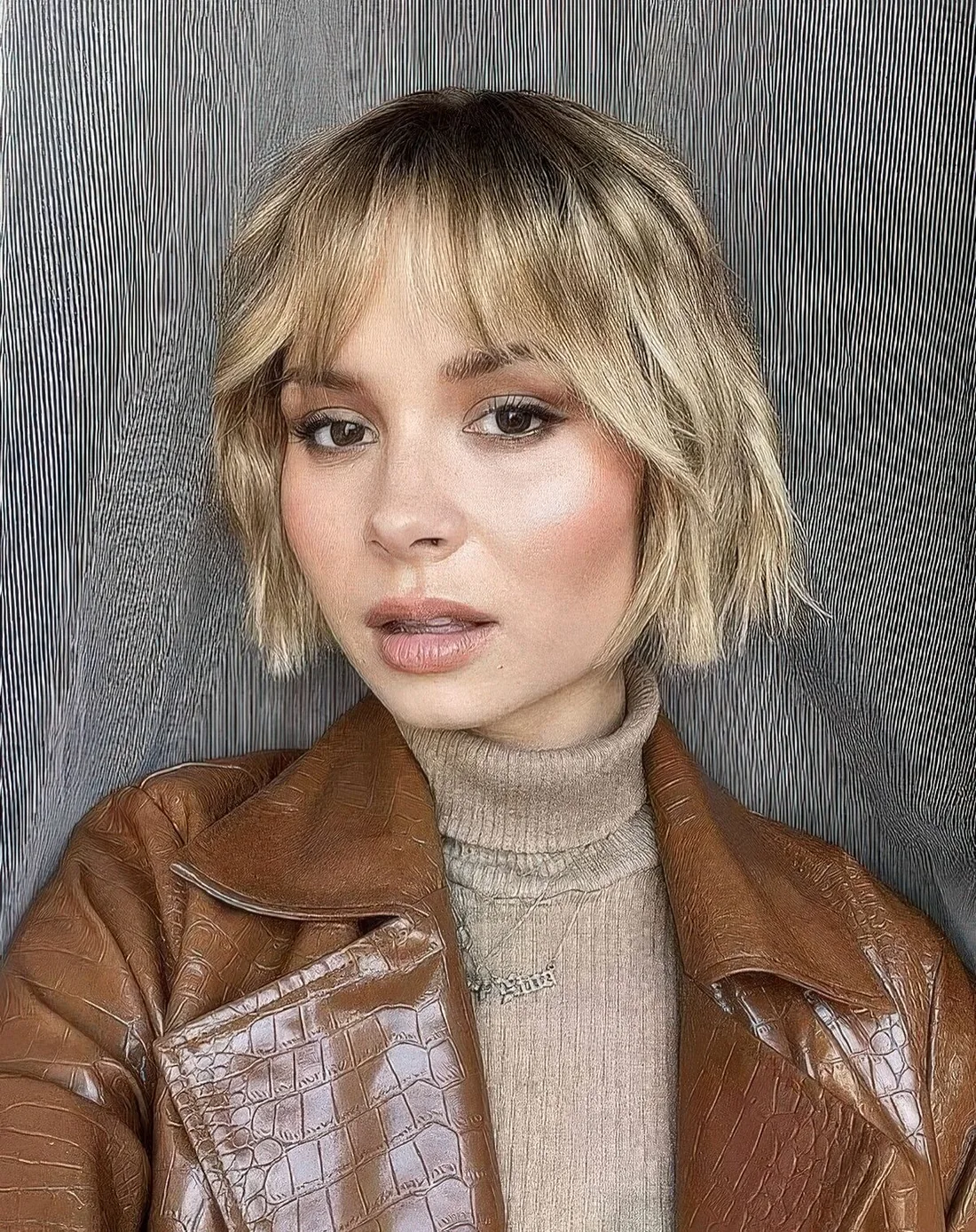 Relaxed blonde wavy jaw-length bob with wispy bangs.