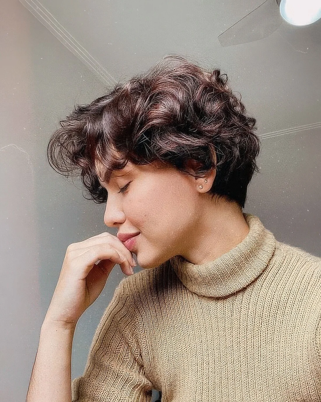 Dark brown wavy and curly pixie with a bit of short bangs.
