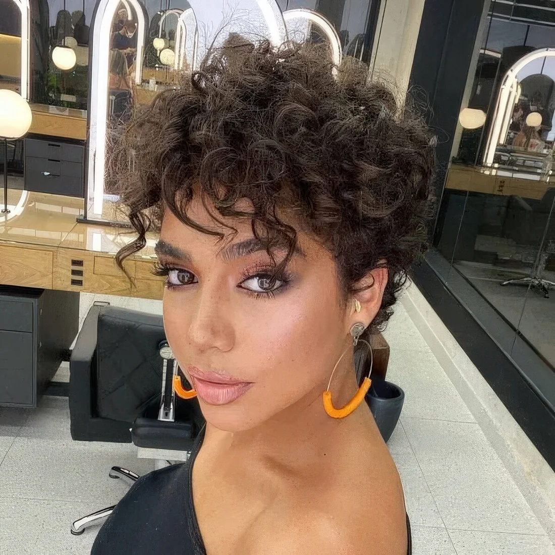 Dark brunette long curly pixie haircut with some volume and bangs.