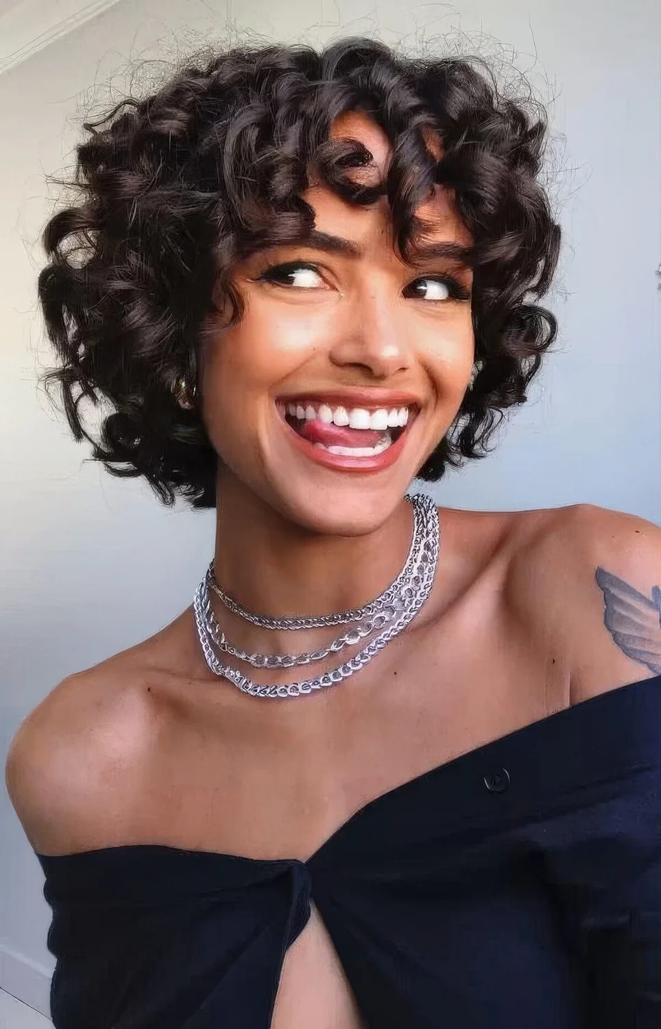 Black chin-length curly bob to pixie haircut with bangs.
