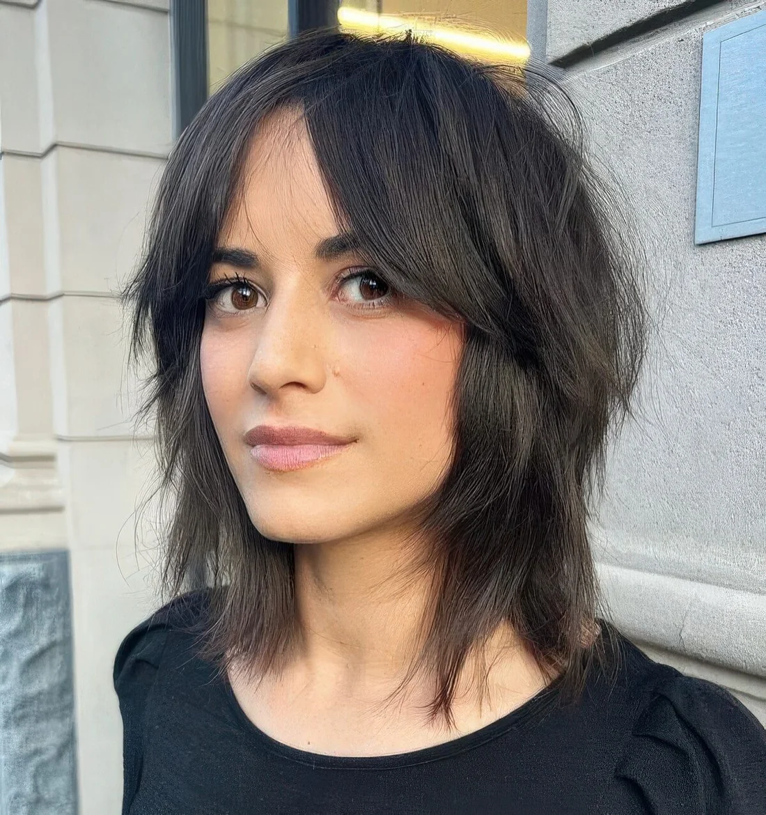 Black shyggy medium-length haircut with short curtain bangs.