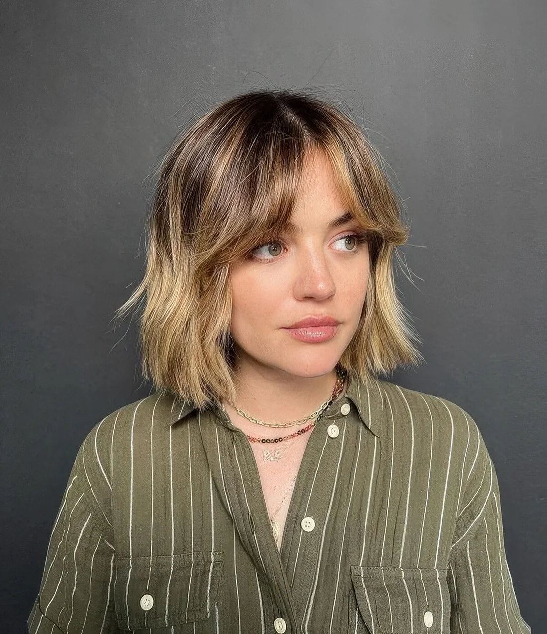 Long blonde bob with a darker root and short curtain bangs.