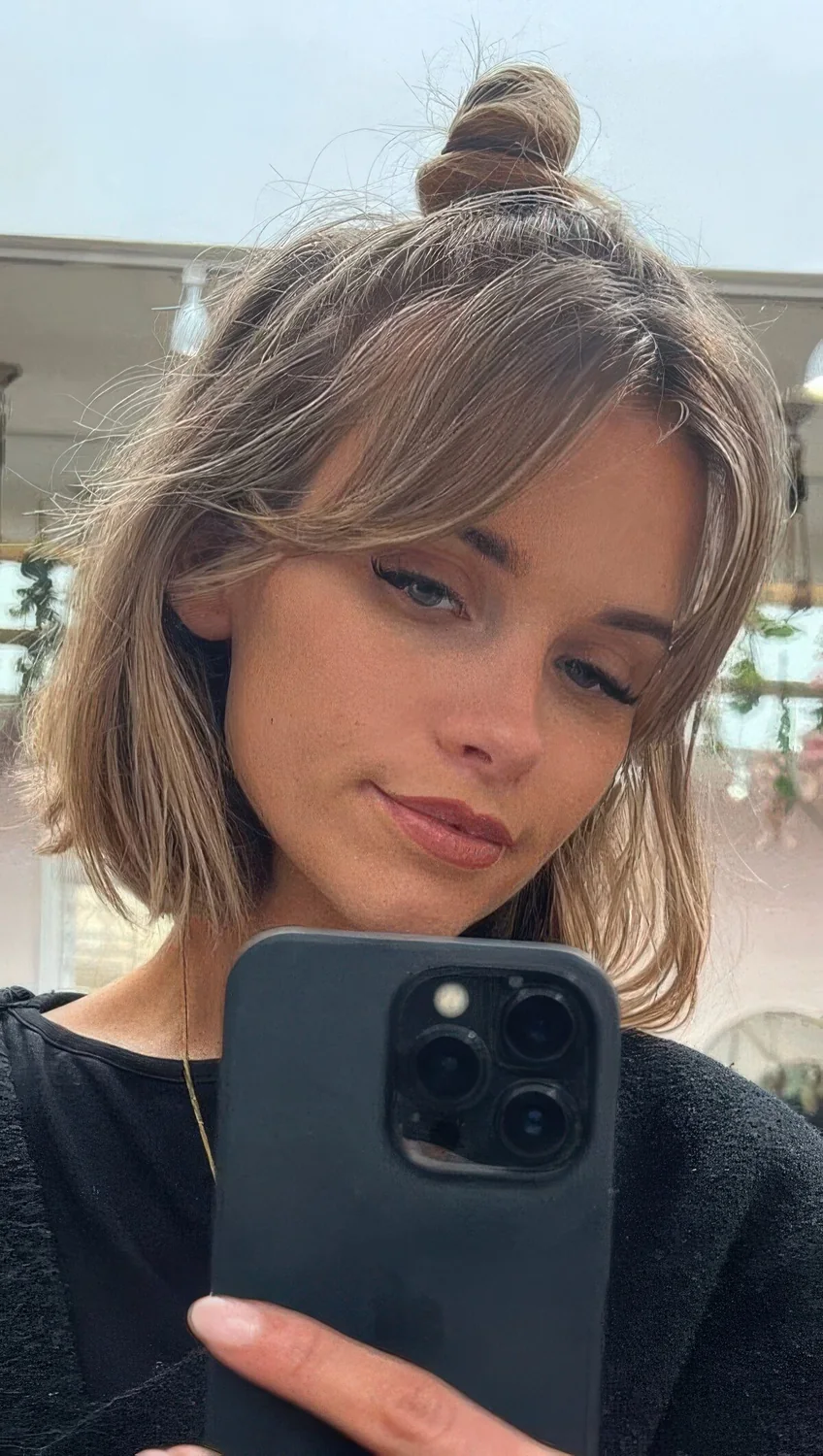 Long blonde bob with a top knot and short curtain bangs that accent the eyes.