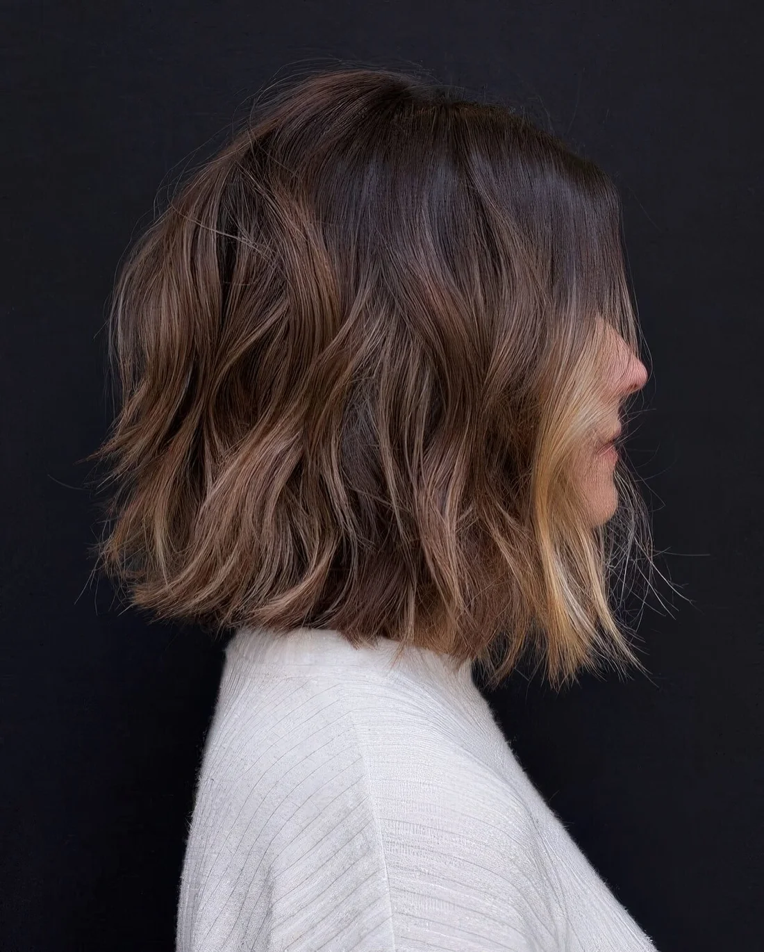 Dark brown bob with a black root, chestnut balayage and blonde money piece to highlight the look.