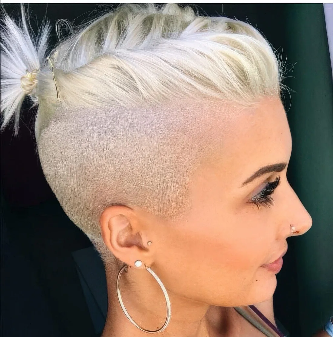 Long bleached blonde pixie with an undercut styled with a little ponytail on top to keep the hair off the face.