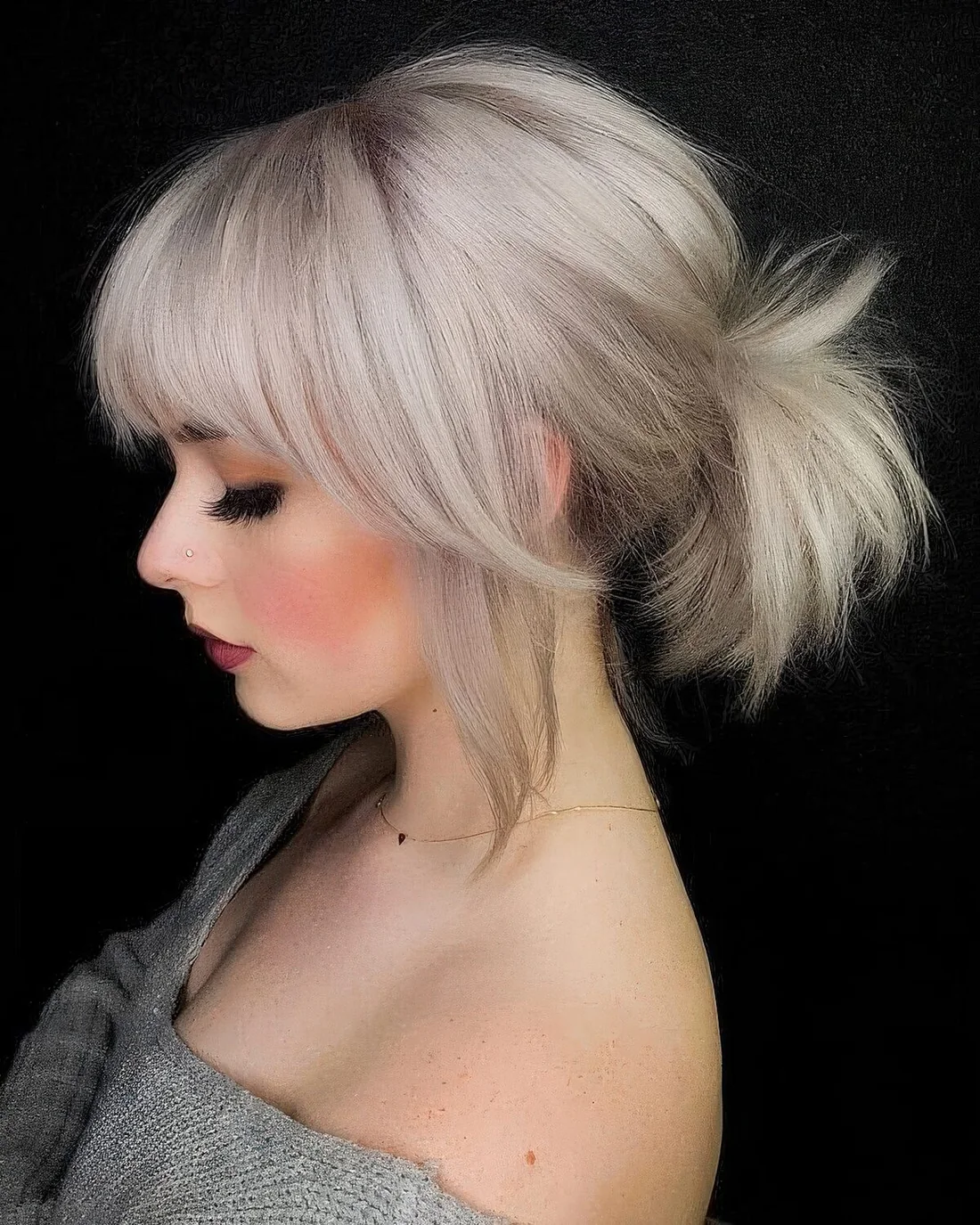 Low bleached blonde ponytail with a bump on top and classic and side bangs.