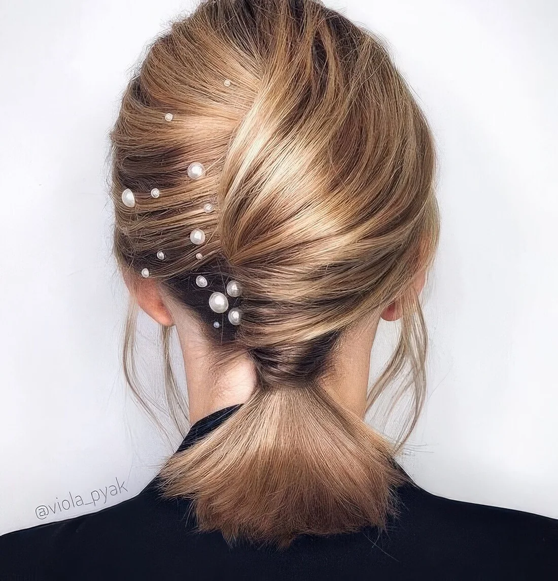 Low ponytail with a twisted chignong and pearl hair pins.