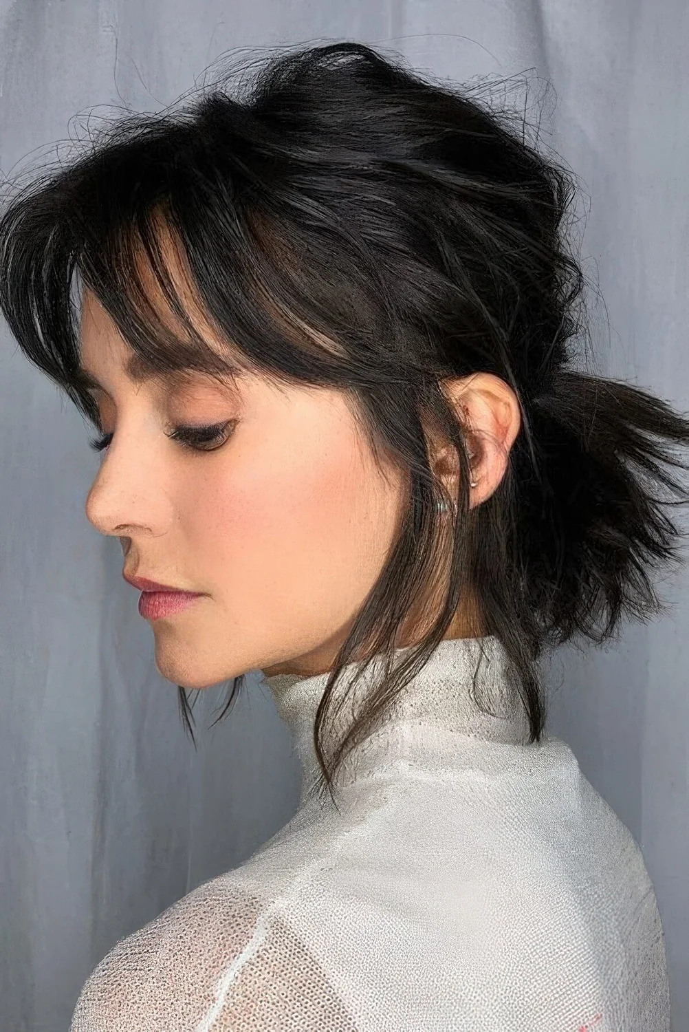 Low textured and volumetric hair styled in a low ponytail, with a messy bump on top and bottleneck bangs.