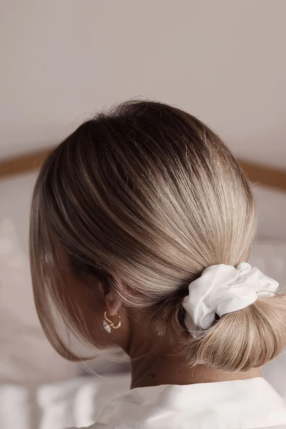 Low updo with a sleek top and a low bun made with a scrunchie and face-framing hair.