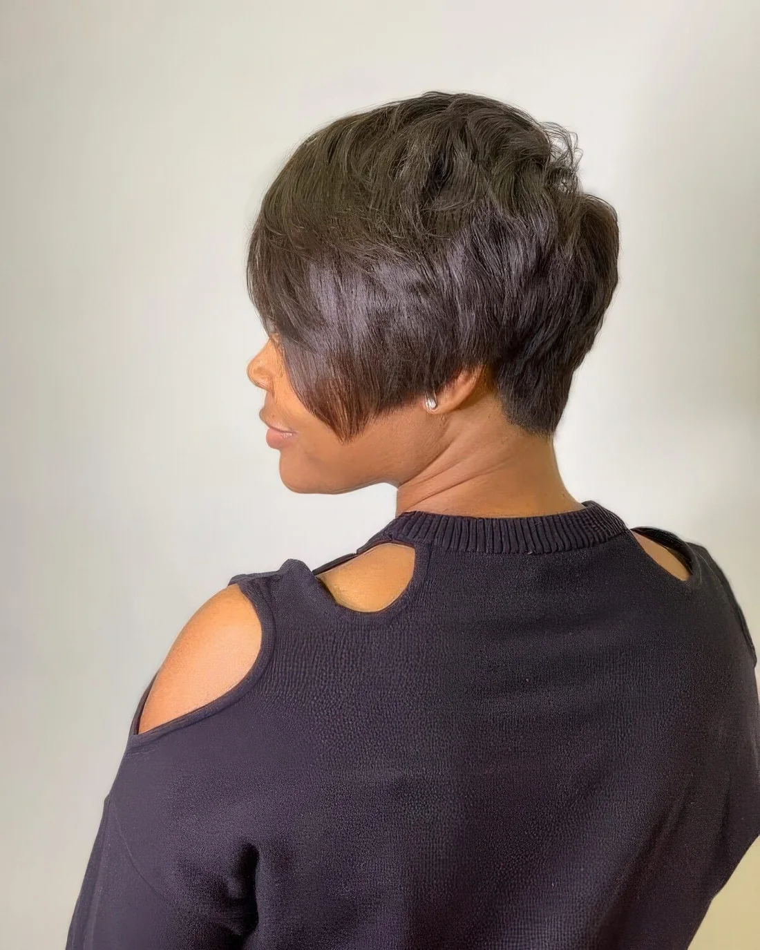 Black long pixie with long side bangs, a lot of layers and the hairline at the back that tapers into a V shape.