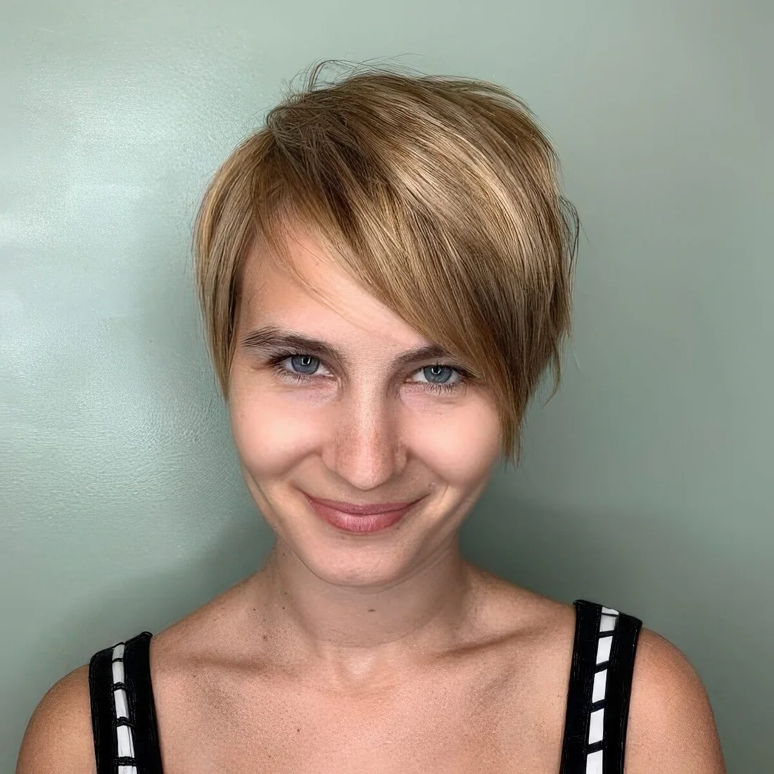 Short blonde pixie with long side swept bangs offers texture for a rugged style and highlights make it dimensional.