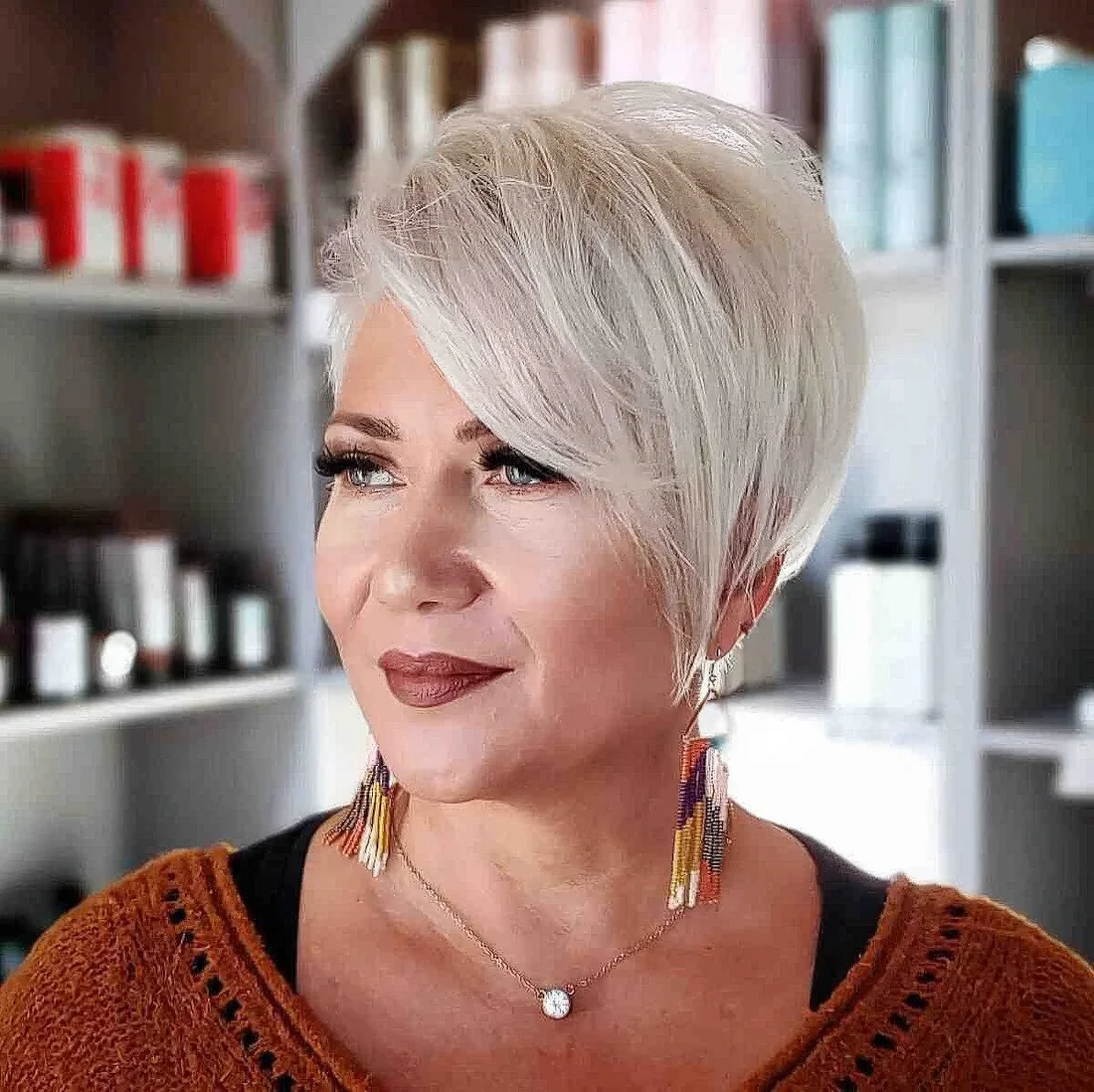 Icy blonde pixie haircut with long side bangs, layers and texture.