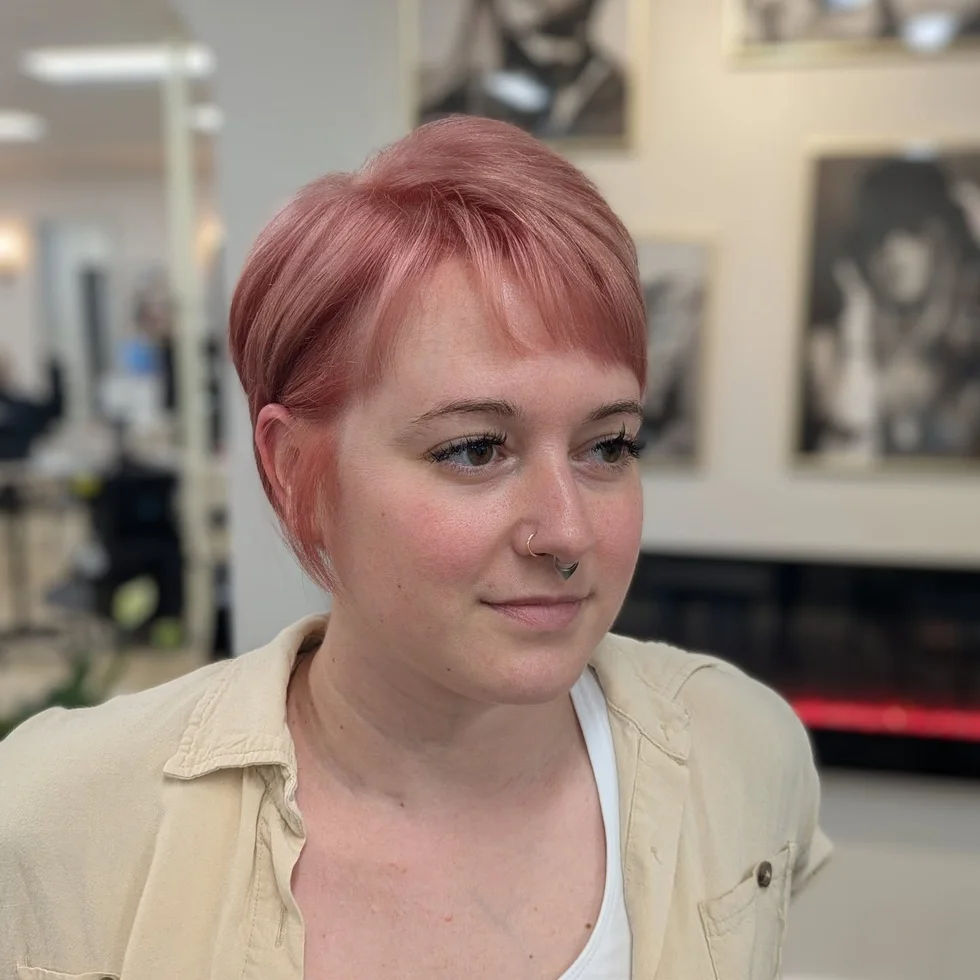 ear straight chestnut pixie with side swept fringe shown as a short hairstyles for thin hair and round face idea, featuring side part, shown in pastel pink cropped pixie