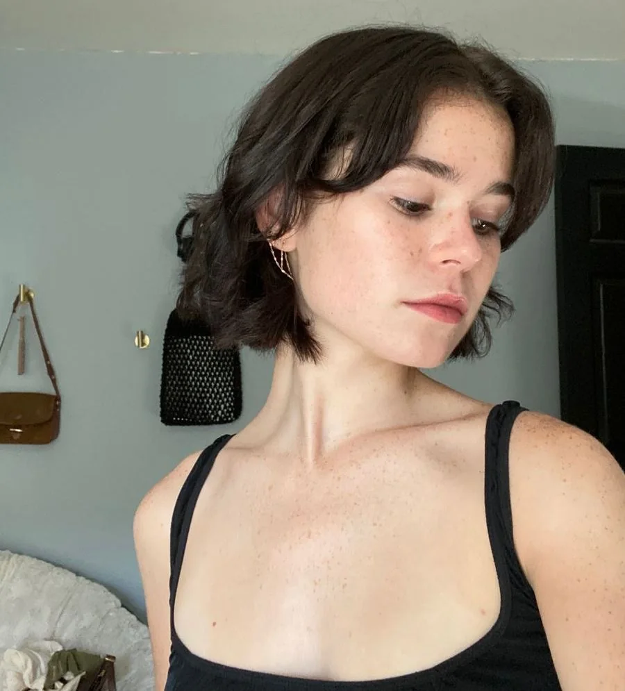 A brunette bob has long curtain bangs, a lifted crown, and ends flicked away from the face