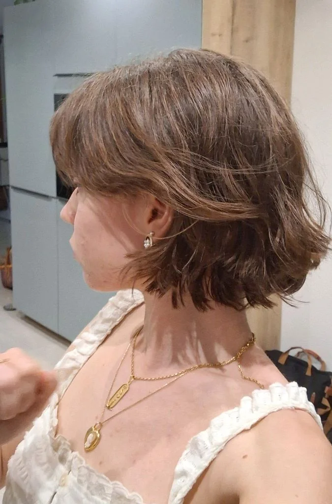 A warm brown bob uses full bangs, feathered side layers, and a softly turned neckline