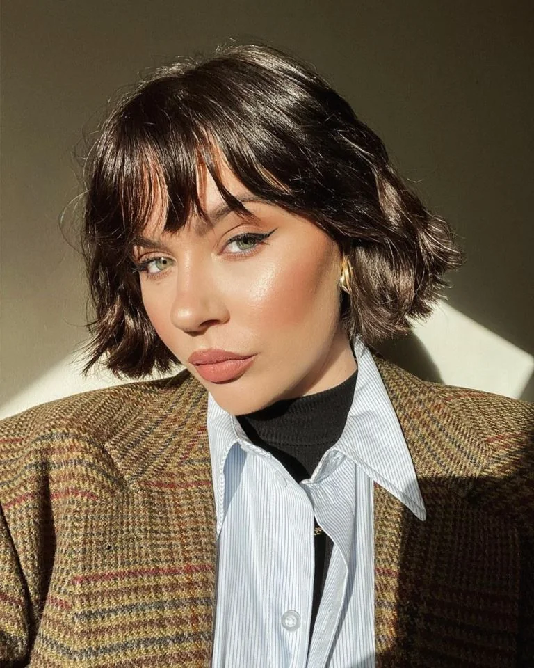 A glossy brunette bob combines wispy bangs with small waves and piecey ends around the jaw